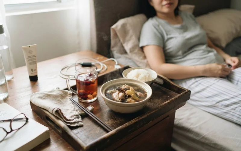 A neatly arranged tray of traditional confinement postpartum meals with rice, soup and vegetables on a clean table setting